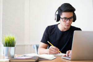 Young collage student using computer and mobile device studying online.